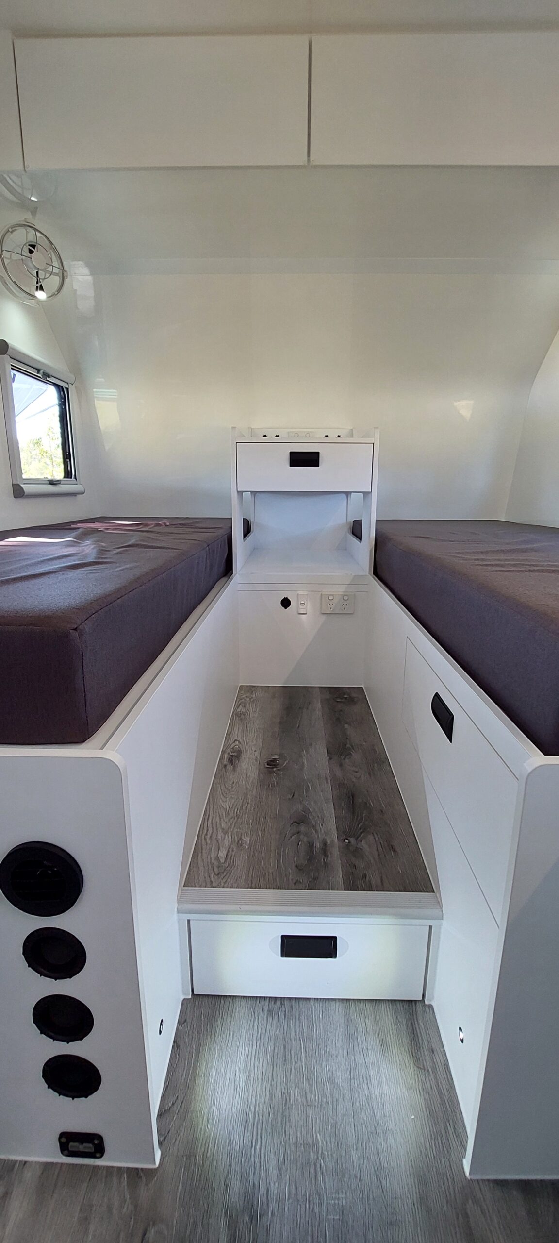 Interior view of a Queensland built caravan featuring two single beds with overhead storage.